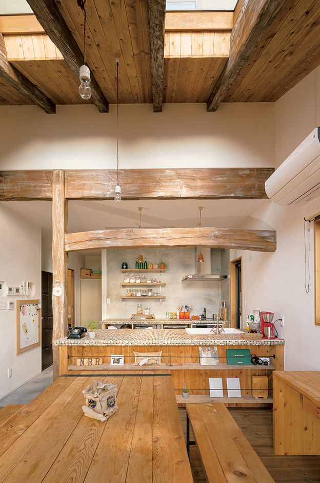 富士ホームズデザイン【デザイン住宅、子育て、インテリア】アンティーク加工した飾り梁とタイル天板が素朴であたたかみのある雰囲気を醸し出すオリジナルキッチン。壁は薪ストーブ のところと合わせてモルタルとした。ダイニングテーブルとベンチは『ラ シュエット フジ』で見た手作り家具をひと回り大き いサイズでオーダー。奥さまの妹さんご一 家と一緒に食事を楽しむこともあるそう