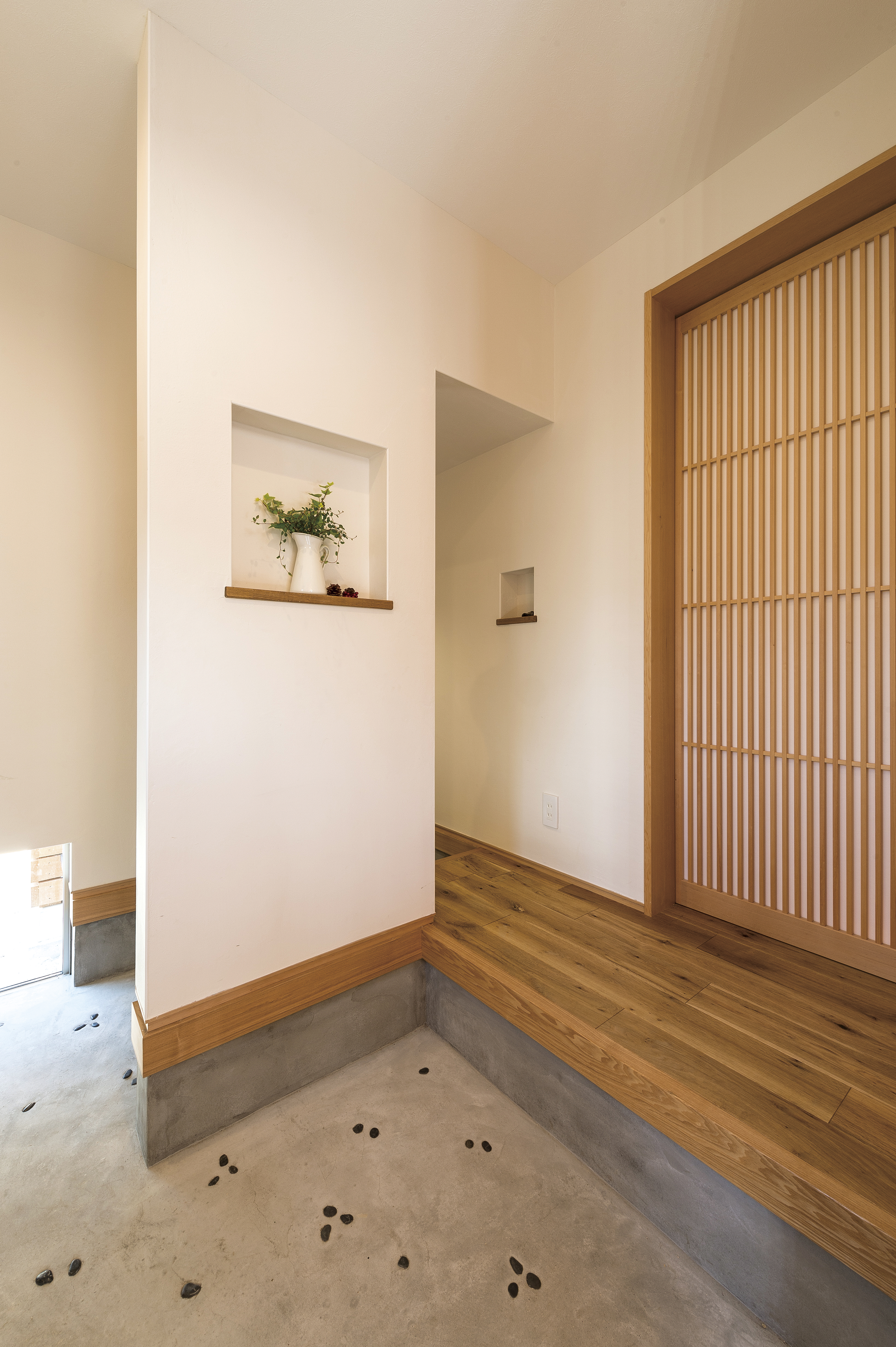斉藤工務店｜自然光が優しく差し込む土間スペース。壁には装飾棚があり、観葉植物が飾られている。シンプルで落ち着いた雰囲気。