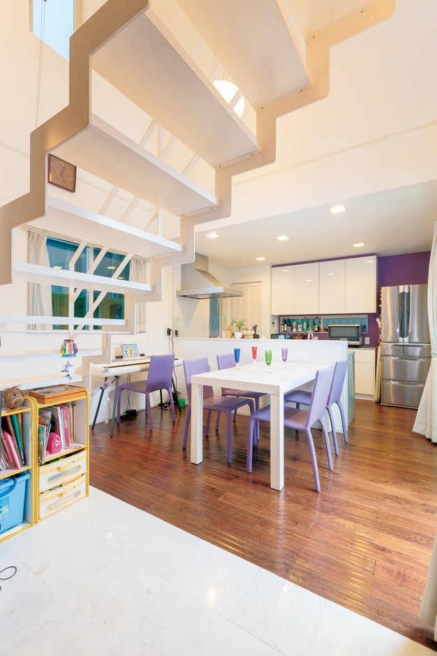 紫色が好きな奥さまの希望で、キッチン背面をアクセントクロスに。『納得』オリジナルのダイニングセットの、紫色の椅子もポイント。階段下の大理石は優雅な印象