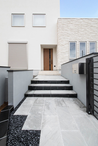 白い建物とのコントラストを考えてデザインされたアプローチ。黒い石やタイルで引き締めている