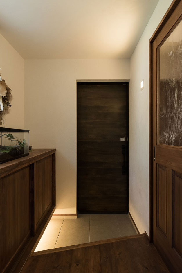 アイジースタイルハウス【デザイン住宅、高級住宅、ガレージ】あえて色ムラを残した扉がかっこいい玄関スペース。足元の間接照明が隠れ家的な雰囲気を醸し出す