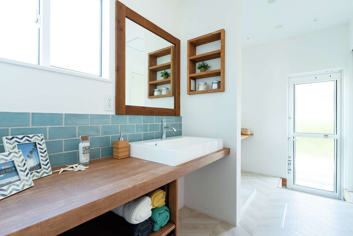 KUREKEN HAUS（榑林建設）【デザイン住宅、省エネ、間取り】海を感じさせる造作洗面。タイルやニッチなど、テイストがまとめられたナチュラルな洗面台は、毎朝気分を上げてくれます。
奥のランドリールームは勝手口やクローゼットにつながる。