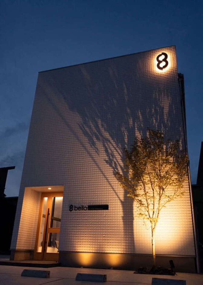 夜間はアッパーライトでライトアップ。照明の灯りで外壁にシンボルツリーの陰影や木製のドアが浮かび上がり、シンプルなフォルムにゆたかな表情をもたらしている