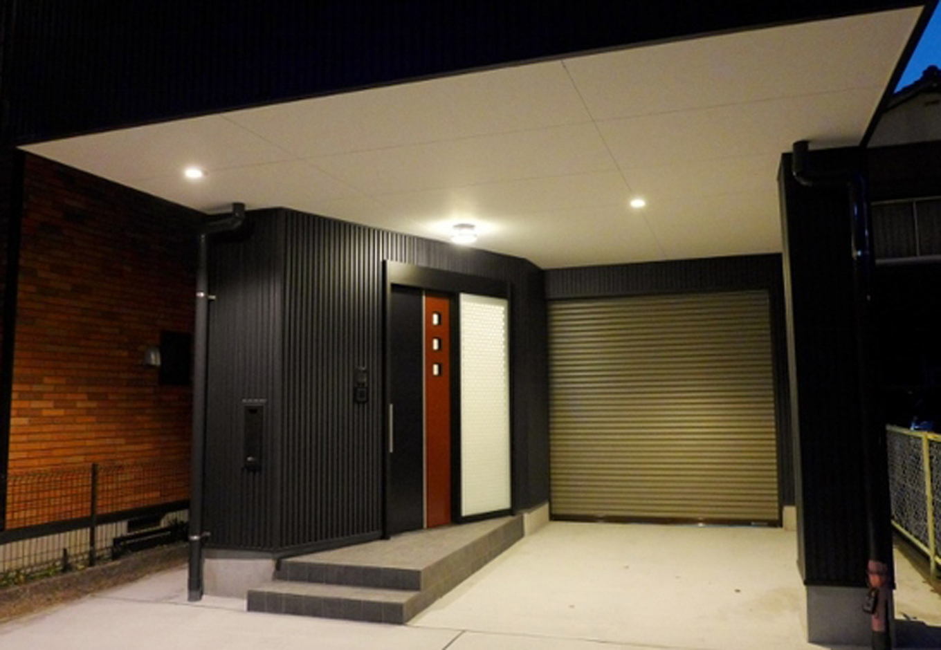 建築システム（狭小住宅専門店）【デザイン住宅、ガレージ、鉄骨鉄筋コンクリート構造】外壁に合わせてインターホンや解錠デジタルボタンも黒。照明や埋め込みポストまで徹底的にこだわり統一。玄関引き戸もブラックですが、赤茶のスリットがアクセントで際立っている