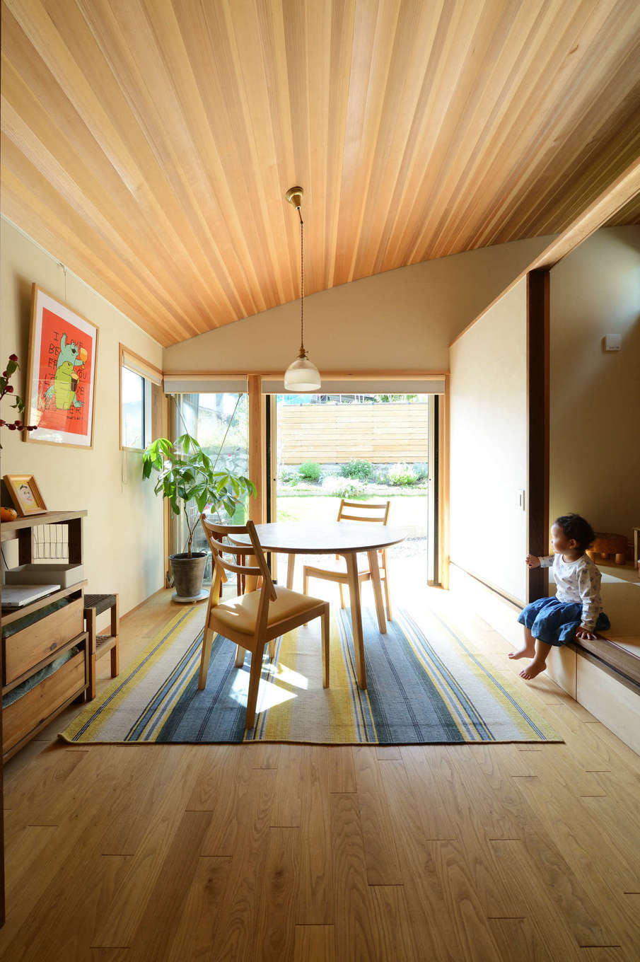 石牧建築【自然素材、狭小住宅、建築家】天井をRにしたことで、奥行きと開放感が生まれたダイニング。椅子に座ると、ちょうど目線と同じ高さに庭の花々が見える。クリ、杉、チェリー、ウォールナットなど、自社工場にストックしておいた多彩な樹種を適材適所に使用。ぽってりとした可愛らしいペンダントライトは、森町在住のガラス作家によるハンドメイド作品