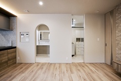 リビング横からランドリーと洗面へアクセスできる動線を確保。シンプルな床材と白い壁が明るさを引き立て、奥にはアーチ状の開口部が特徴的なデザインが施されている。