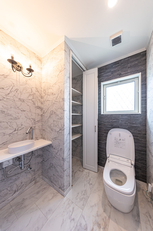 モダンでスタイリッシュなデザインのトイレ空間。大理石調の壁面と床が高級感を演出し、ダウンライトが落ち着いた雰囲気を提供する。