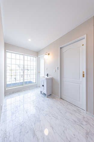 明るく開放的な洗面スペース。大きな窓から自然光が差し込み、白を基調にした内装が清潔感を演出している。