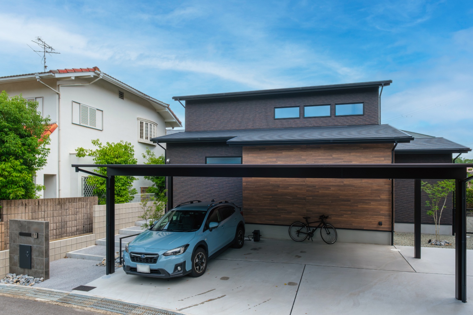 新栄建設｜シックな色合いのモダンな外観が特徴の住宅。カーポートには車と自転車がきちんと収まり、機能的なデザインで快適な暮らしを支える。