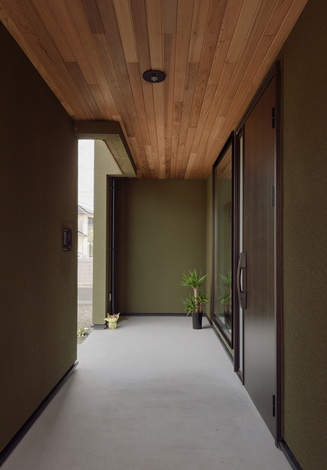 モスグリーンの外壁の裏面には玄関ポーチを横長に広々と確保。フィックスの窓の奥に見えるのは土間のディスプレイコーナー