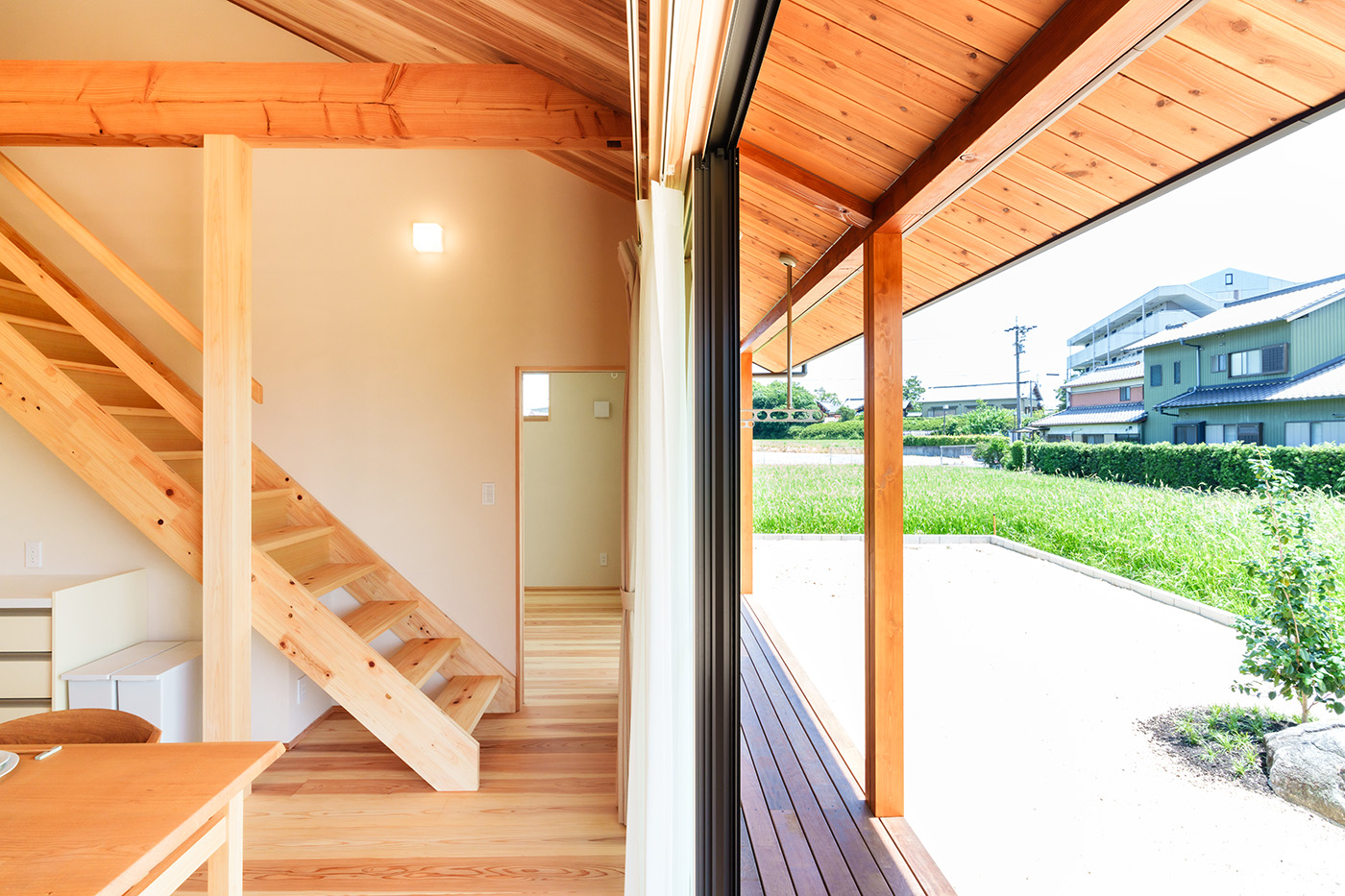 アンシンハウズ【自然素材、間取り、平屋】リビングの掃き出し窓を開けるとウッドデッキ、庭へとつながる。杉の天井が外まで連続しているので、より外と中との一体感を得ることができる。深い軒が夏の直射日光を遮り、太陽高度の低い冬は、キッチンの奥まで光を届けてくれる