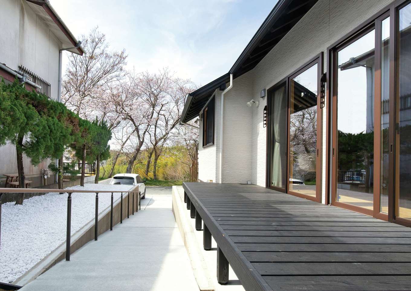 サイエンスホーム【趣味、自然素材、平屋】将来を考えスロープを希望した。広いデッキはご近所さんとの交流の場にも。外観カラーは奥にそのまま残された車庫とのバランスも考慮