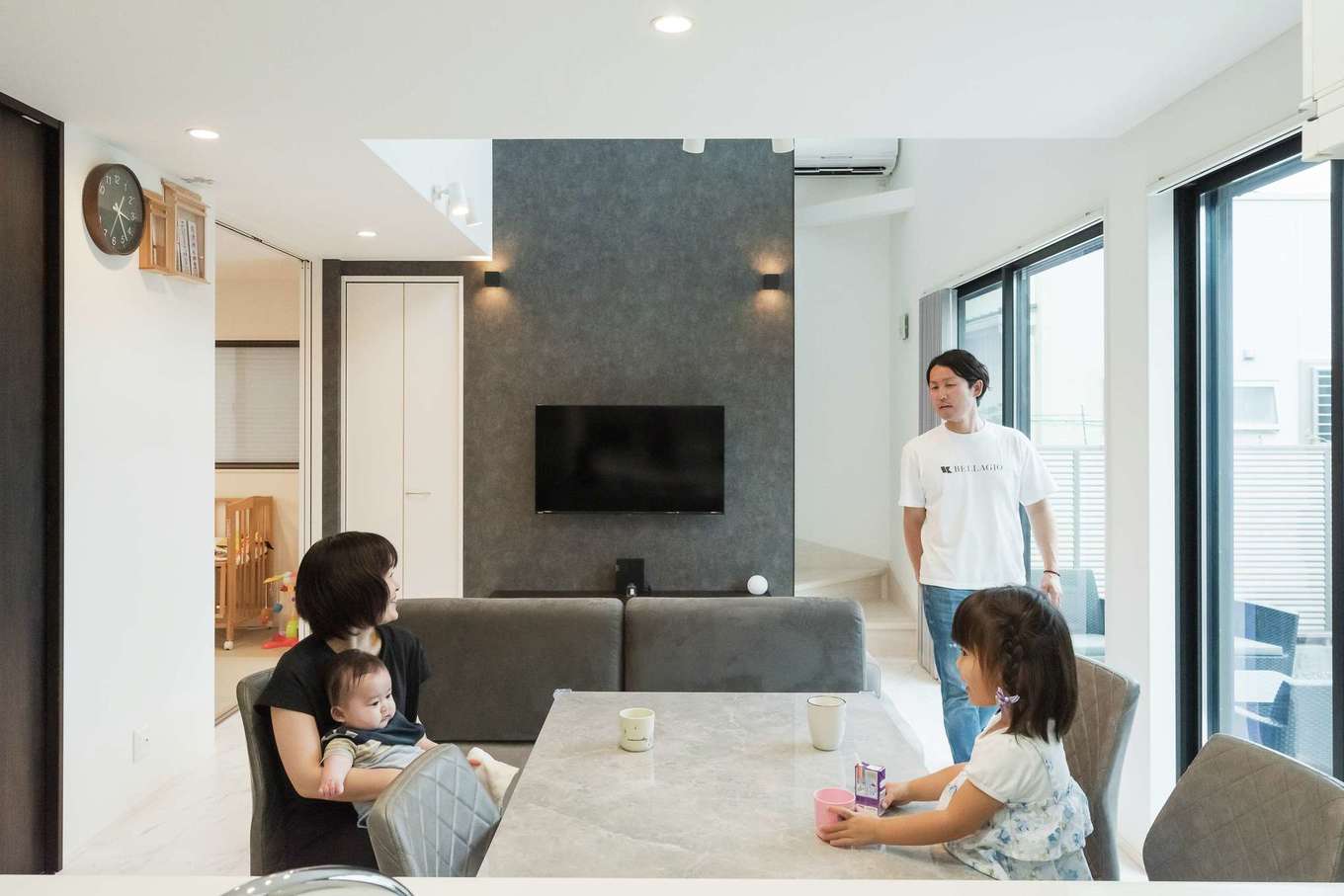 HAPPY HOUSE（山田工務店）【デザイン住宅、子育て、間取り】キッチンからLDKを見通す。テレビ背面の壁にアクセントのクロスを選び、大らかな空間に落ち着きが添えられた。階段下を活用した収納がLDKのキレイに貢献する