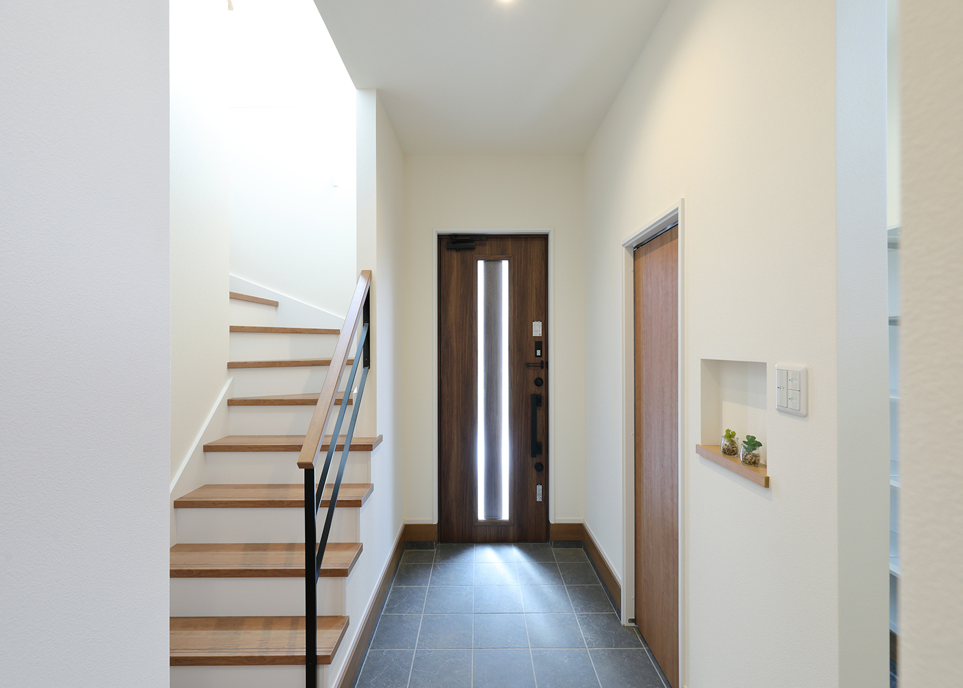 丸昇彦坂建設【子育て、収納力、間取り】シューズクローク付きの玄関。ブラックアイアンの階段手すりが空間を引き締めている。玄関ホールには衣類をしまう収納も確保。階段の向かいに洗面スペースがあるので、帰宅してすぐに手洗いができる