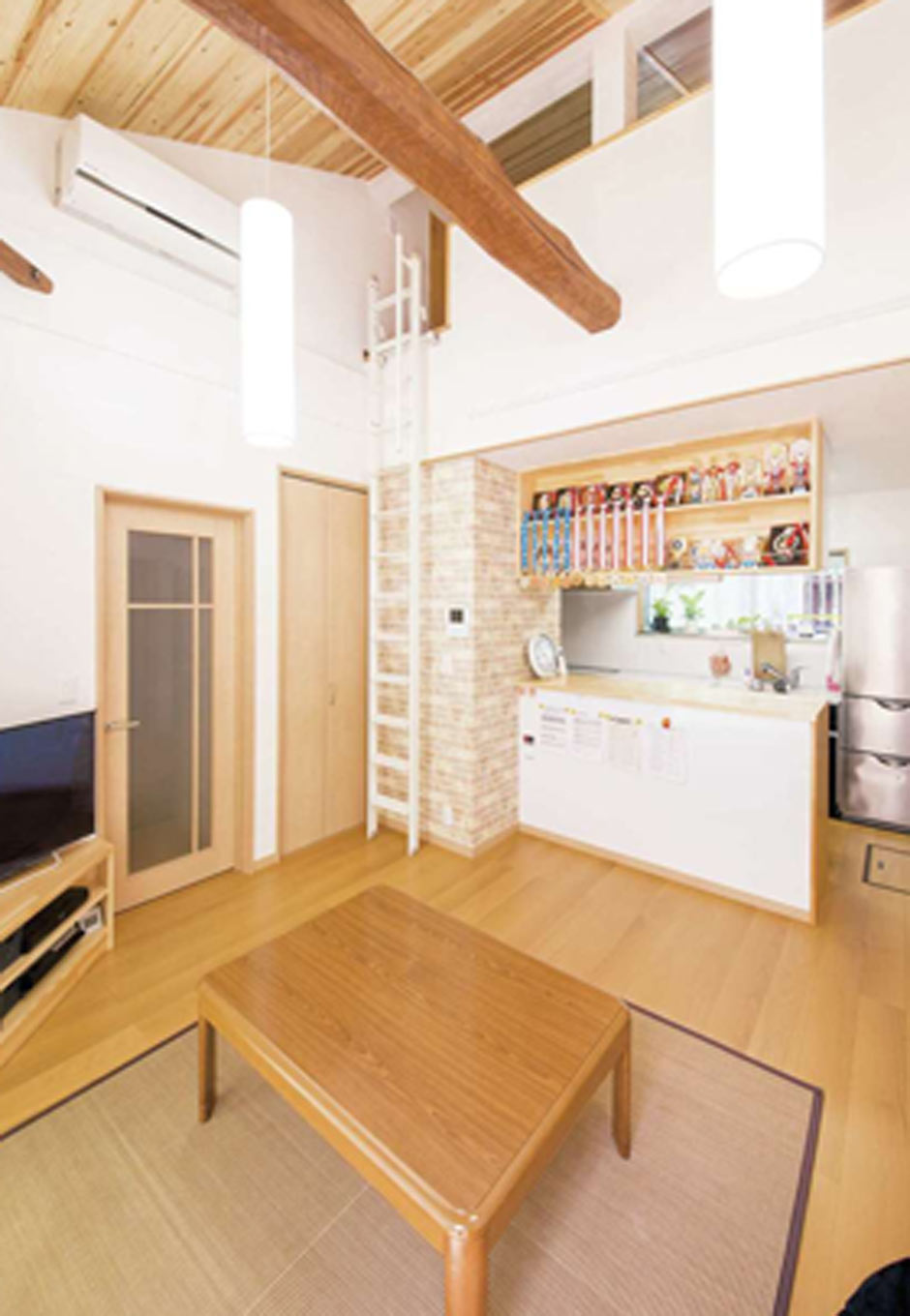 内田建設｜子世帯のLDKは勾配天井を活かした大空間。梁は塗り替えをして現しに。吊り戸棚の背面に取り付けた飾り棚には子どもたちの空手のメダルがずらり。左手のドアの先に子ども部屋へ上がる階段がある