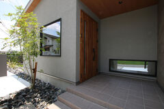 グレーのモダンな色合いでコーディネートされた玄関まわり。アプローチにはシンボルツリーが植えられており、玄関の中から四季折々の変化を楽しむことができる。玄関は上部が庇になるように位置が考えられており、外の天候を気にすることなくドアを開けられる