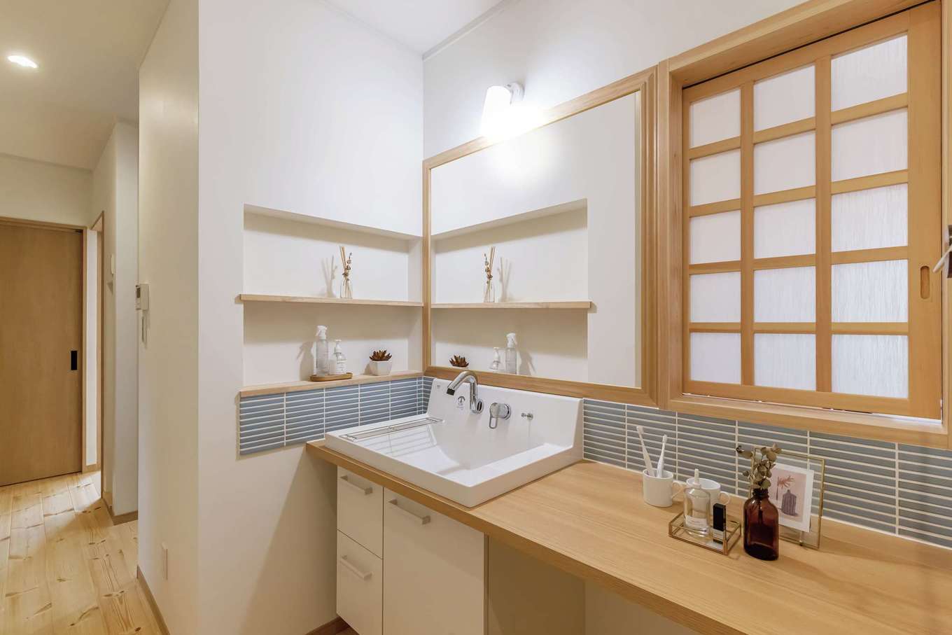 住まいるコーポレーション【自然素材、間取り、平屋】洗面スペースには、LDKの小上がりに通じる風通し用の障子戸を設けた。白を基調とした空間にタイルをあしらい、カウンターは広めに確保。ニッチは歯ブラシや化粧品などを置いたり、フレグランスや小物を飾ったりと、使い方いろいろ
