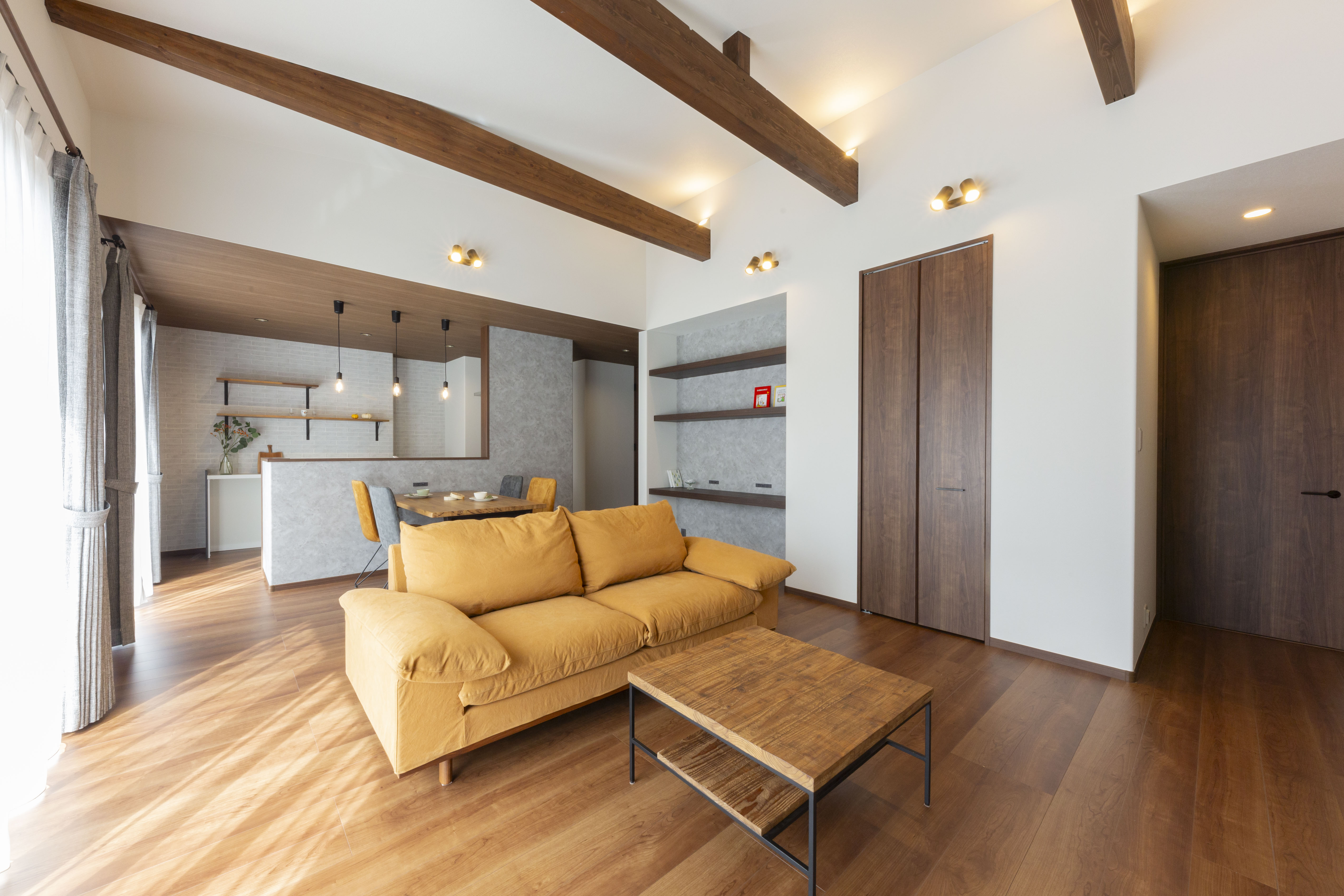 感動ハウス｜広々としたLDK空間。温かみのある木の床と天井の梁がアクセントになっているリラックスした雰囲気。ソファやテーブルが配置され、家族が集う場として最適な設計。