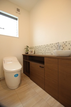 ナチュラルな色合いのトイレ空間。木製の収納とシンクが備え付けられ、モザイクタイルの壁がアクセントとなっている。