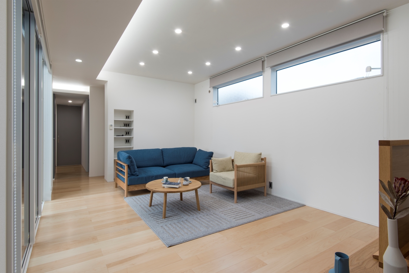 リンクホーム【デザイン住宅、間取り、平屋】17畳のリビング。白と木目を基調とした空間に青いソファが差し色に。プライベートを重視して、窓の大きさと位置に配慮した