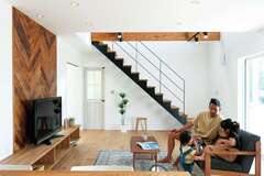 吹き抜けの開放感と無垢オークが放つぬくもりをアイアンの階段が引き締める。造作テレビ台の背後に斜めに張られたタモは、1枚ごとアンティーク加工を施してからヘリンボーン調にすることで、より本格的な雰囲気を演出できるようにこだわったもの。視線を落ち着かせつつ、空間のアクセントになっている。