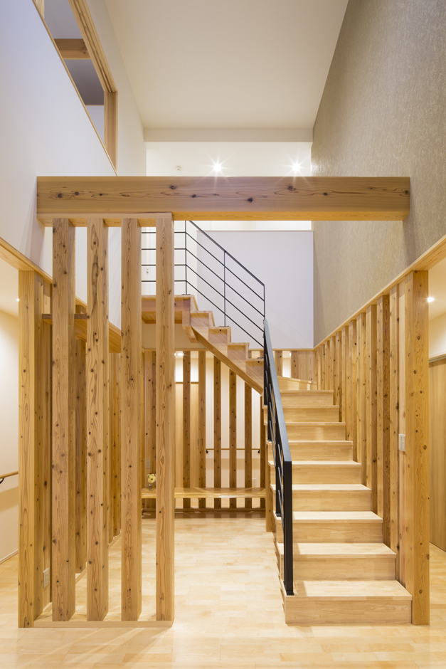 一級建築士事務所 GO_AN (ゴアン)【デザイン住宅、和風、建築家】建物中央にある吹抜状の杉柱に囲まれた階段室。杉柱の隙間から奥の空間が見えることで閉鎖感がなくなり、空間全体の一体感が生まれた。1階の床暖房やペレットストーブで暖められた熱を2階のホールやＬＤＫへ伝える役目もしている