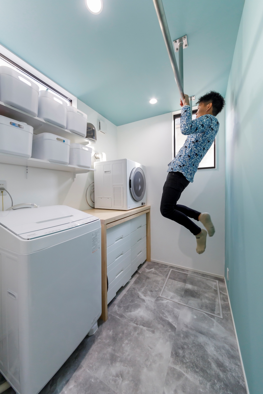nattoku住宅【デザイン住宅、子育て、間取り】洗濯を完結するランドリールームは奥さまのご希望により、さわやかなターコイズブルーでコーディネート。乾燥機の台は造作で、引き出し式の作業カウンター付き。衣類を畳んだり、アイロンを掛けたり、日々の家事を快適にしてくれる。室内干し用のバーは、ご主人の懸垂トレーニングにもなるハイブリッド仕様