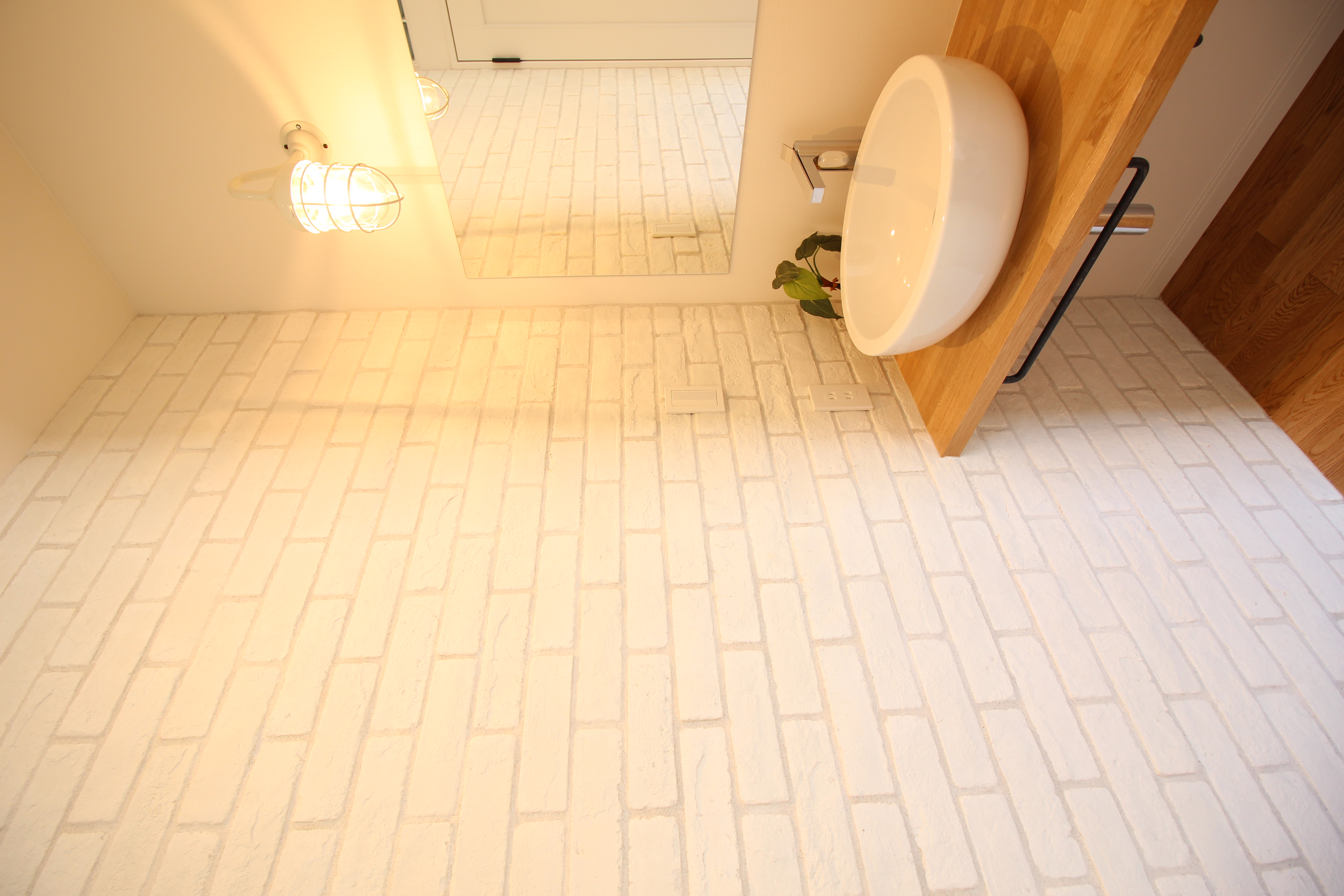 小野田産業～designers house project～｜シンプルでモダンなデザインの洗面スペース。白いレンガ調の壁が清潔感を引き立て、木のカウンターがナチュラルな風合いを添えている。
