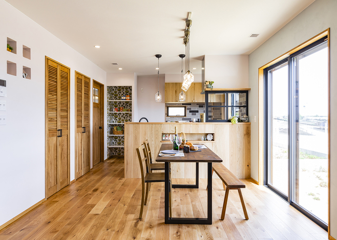 無垢材の床と漆喰の塗壁、木製キッチンを組み合わせたLDK。キッチンの真横に水回りへつながるドアがあり、奥に洗面脱衣所から浴室、ランドリールームまでがまとまる。料理中もコンロ前のガラス窓から、家族の様子がわかるつくり