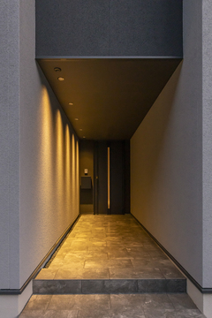 壁面を照らすスポットライトに導かれるように玄関へ。長いアプローチで特別感を演出している