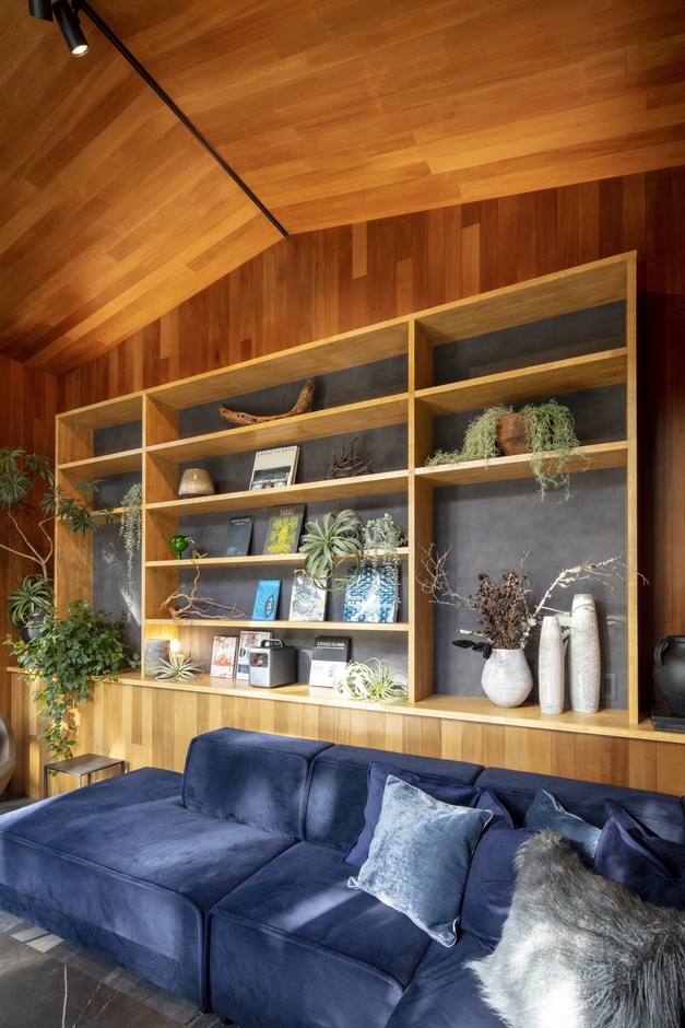 木の温もりを感じるリビング。シェルフには観葉植物やアートがディスプレイされ、青のソファがアクセントとなっている。リラックスした空間が広がる。