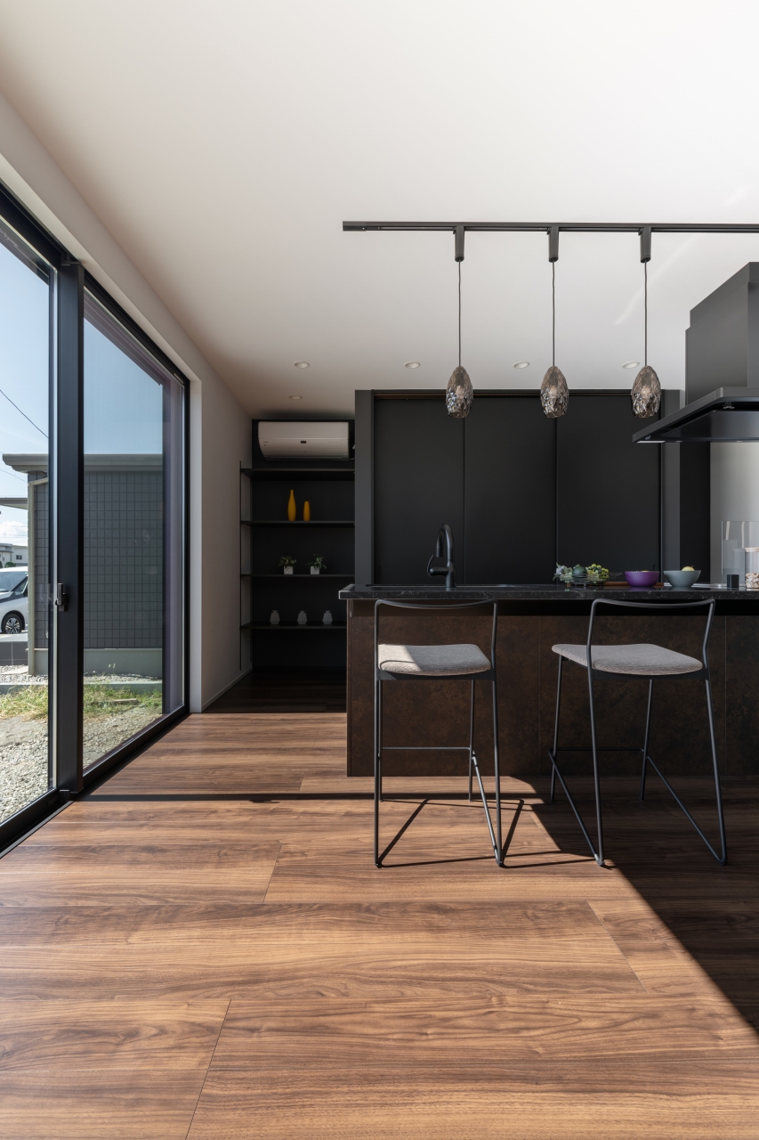 サンジョーホーム｜モダンでシックなキッチン空間。広々としたカウンターにはバーチェアが置かれ、開放感のある大きな窓から自然光が差し込む設計となっている。