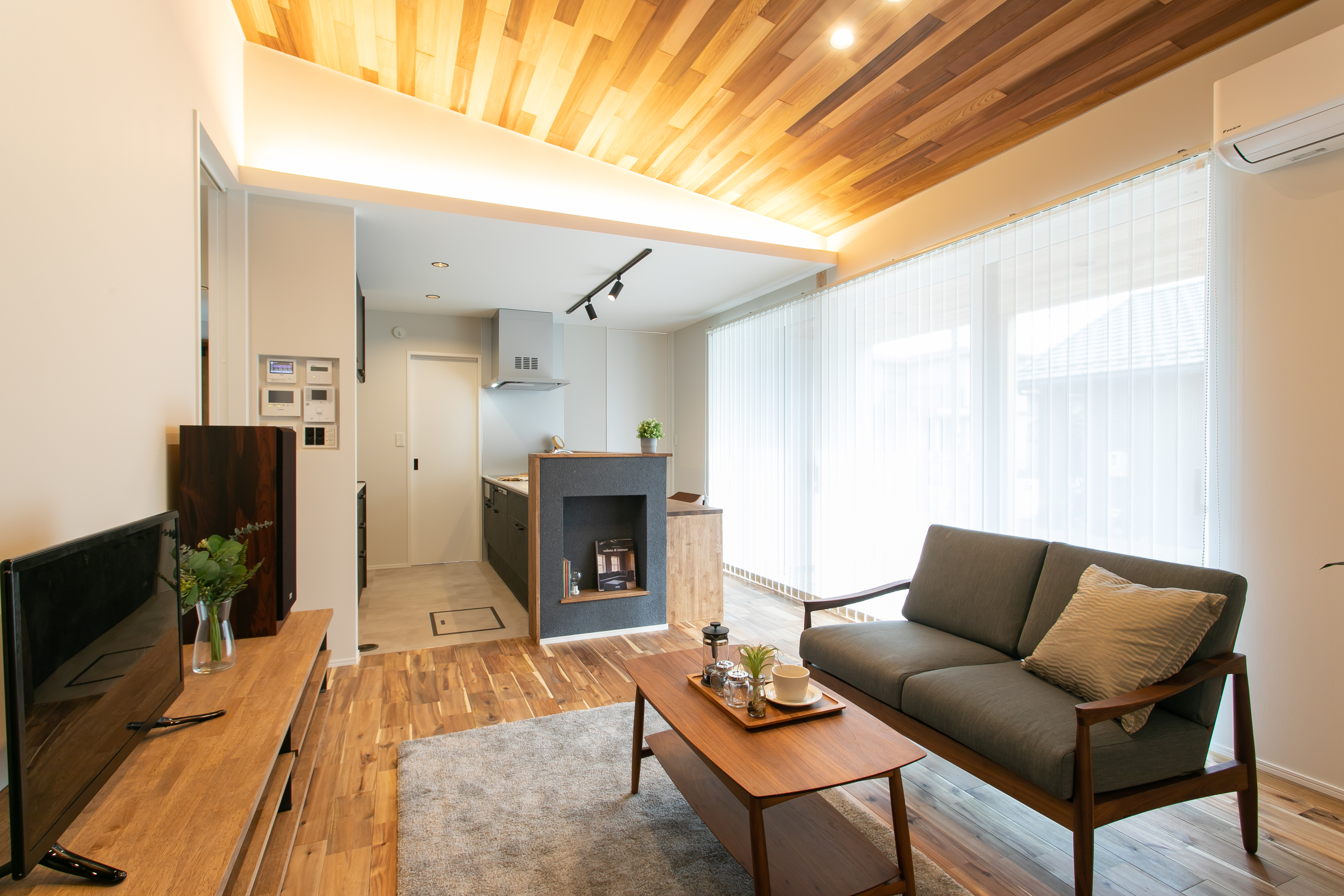 HOME CRAFT｜天井にウッドパネルを使用した温かい雰囲気のLDK。広い窓から自然光が差し込み、明るく開放感がある。モダンなインテリアがリラックスできる空間を演出している。