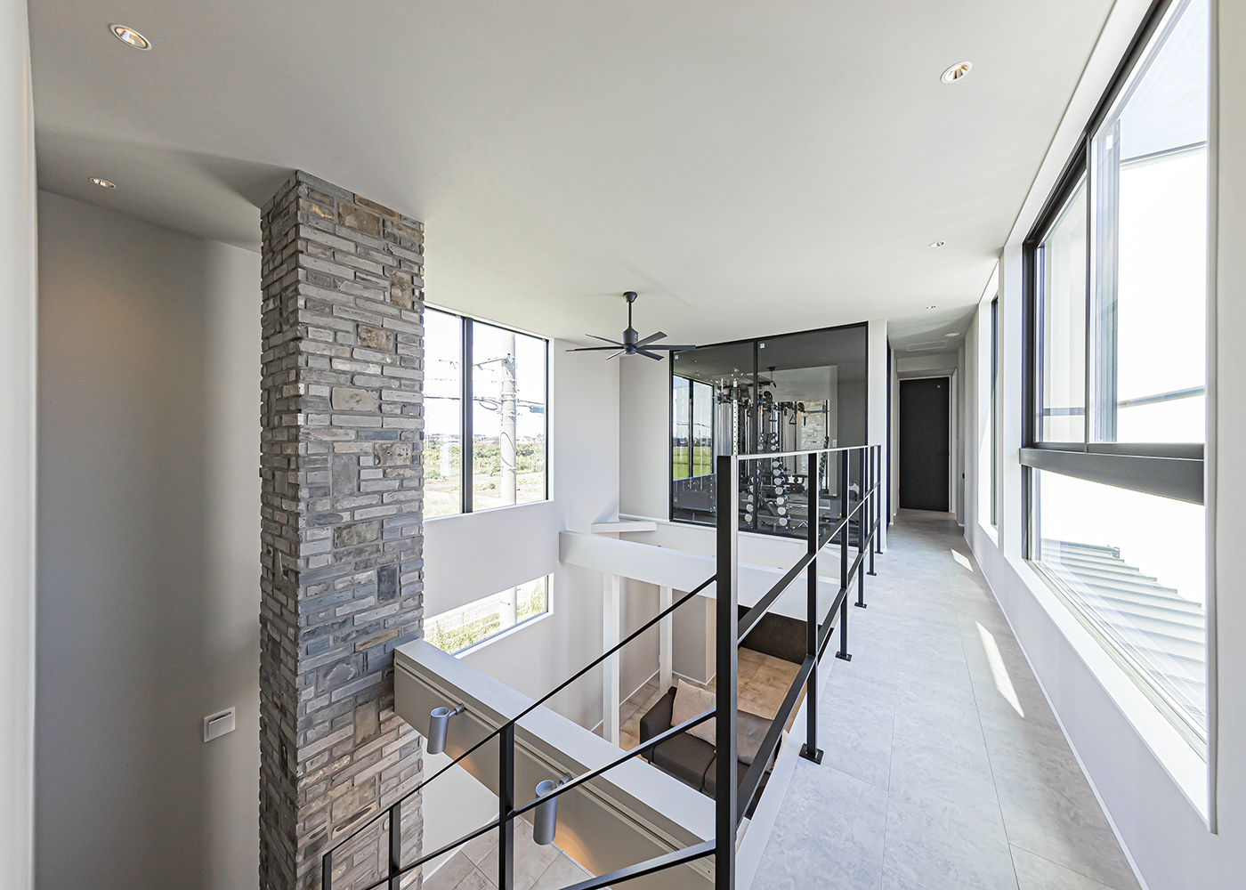 ARRCH アーチ【デザイン住宅、高級住宅、建築家】吹き抜けを貫く石張りの通し壁が広い空間のアクセント。廊下からの眺めも開放的で、住宅とは思えないほどのスケール感