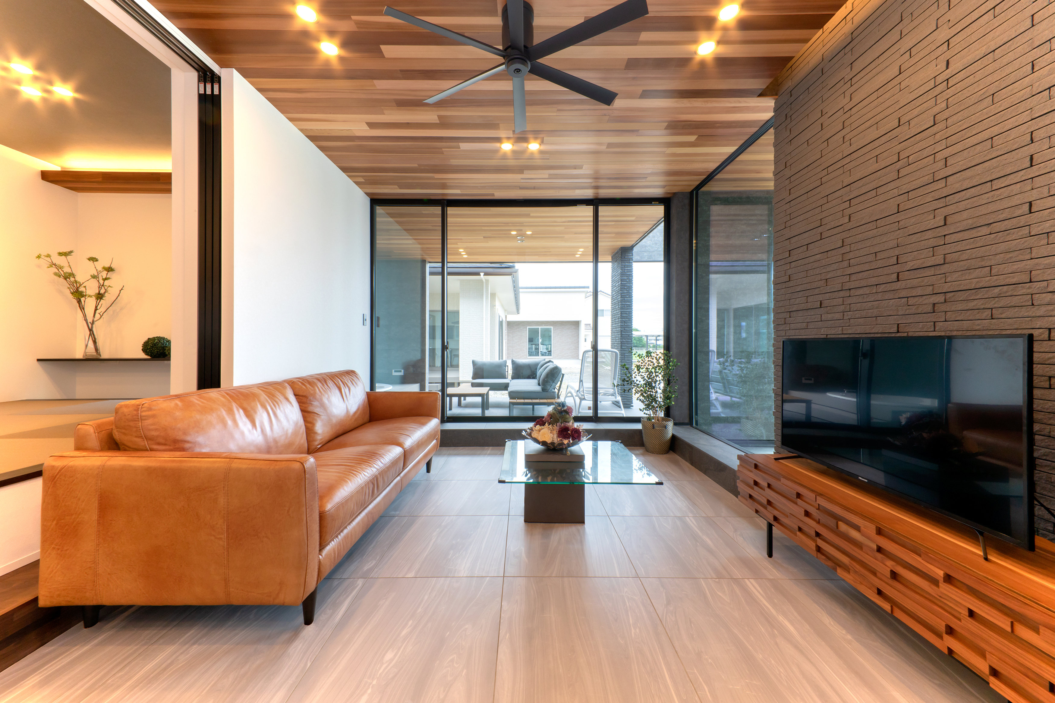 REIWA HOUSE（令和ハウス）｜リビングの天井まで張ったレッドシダーをテラスまで延長。
床も色違いのタイルで揃えた。
リビングは天井まで届く高窓を採用し、外とのつながりが一層感じられる。