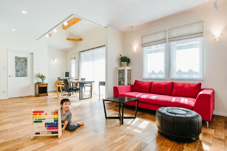 ナカゴミ建設【収納力、間取り、趣味】白を基調とした開放感あふれるLDK。赤いソファが差し色に。肌触りのいい床は無垢のウォールナットで、経年変化も楽しみ