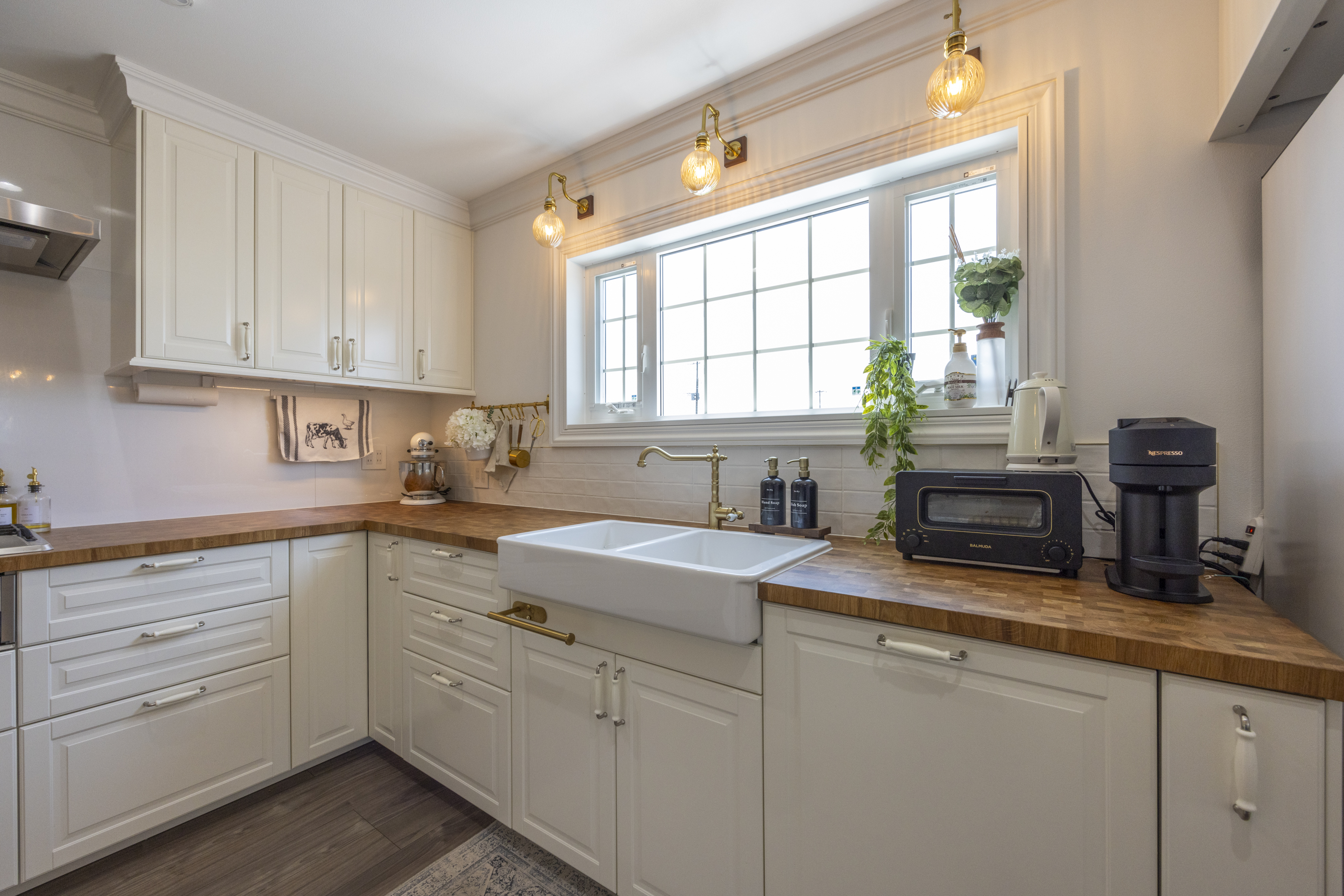 広島建設 セナリオハウス｜カントリー調で白を基調とした明るいキッチン。木製のカウンタートップやペンダントライトなど、こだわりがたくさん詰まった空間となっています。