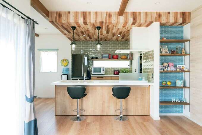 絶妙のクロス選びで、フレンチカジュアルテイストのキッチン周り。ギリギリまで悩み抜いた背面のタイルも奥さまのお気に入り。左奥にダイニングがある。キッチンと横並びの配置で家事動線を短くした