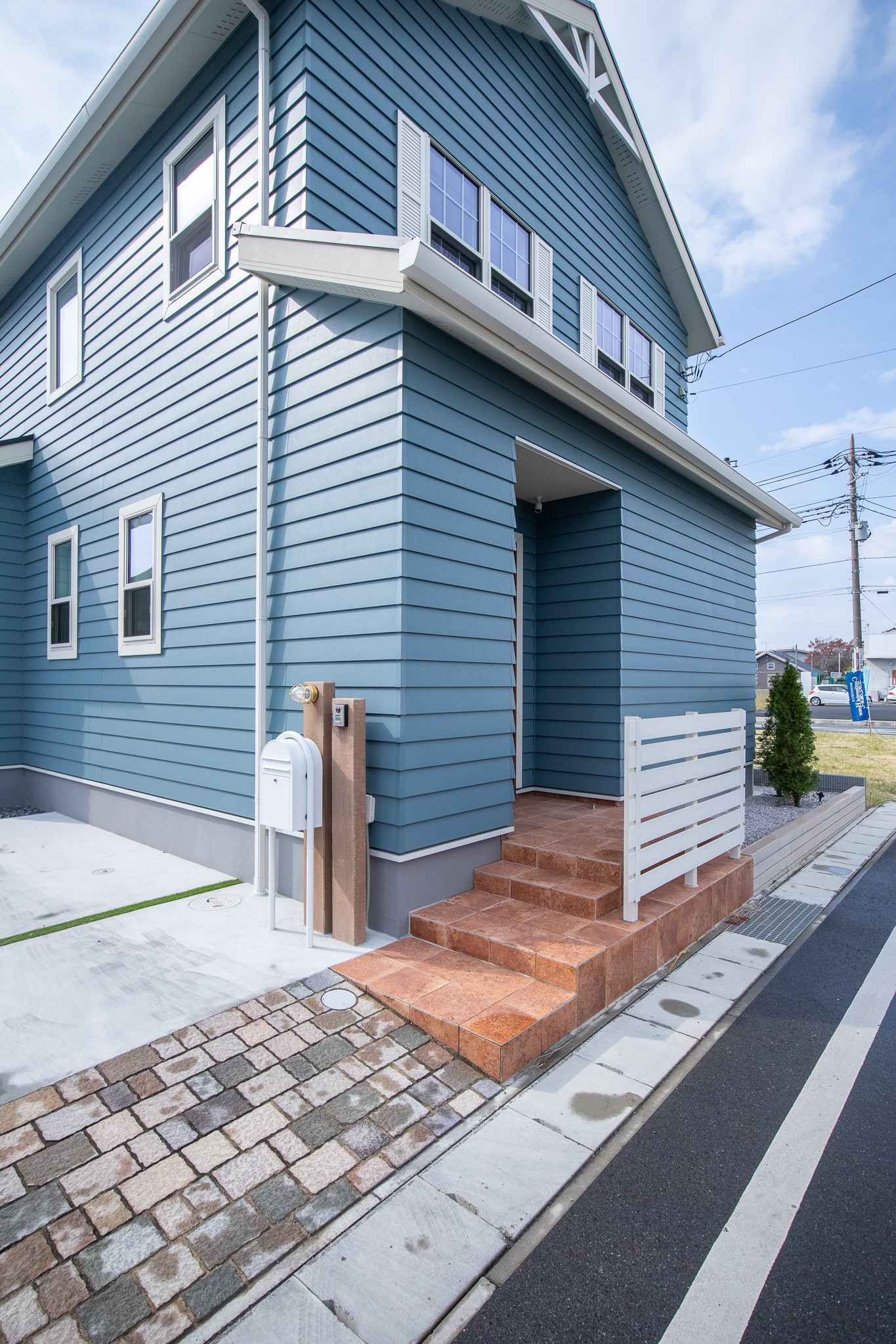 コンチネンタルホーム｜鮮やかなブルーの板張りの外観が印象的な住宅。レンガ色の階段と白のバルコニーがアクセントとなり、調和の取れたデザイン。