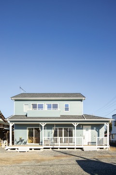 青空に映える可愛らしいブルーのラップサイディング住宅の外観。広いカバードポーチが特徴的である。