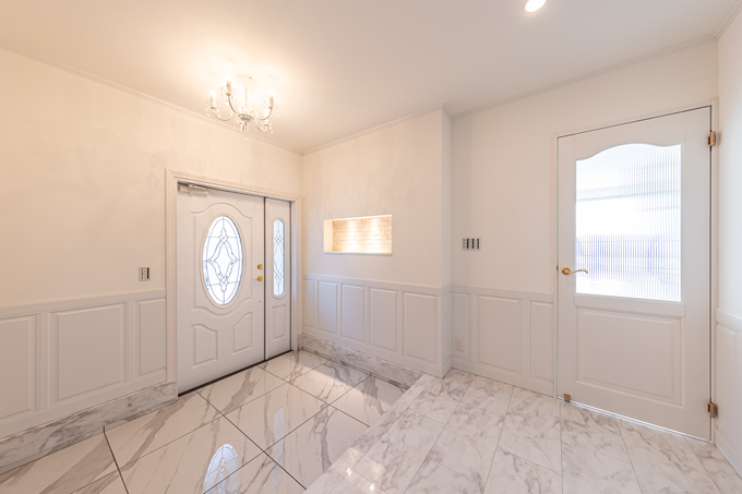 大理石の床が印象的な玄関ホール。明るい色合いの壁とシンプルな照明が調和し、開放感のある空間を演出している。
