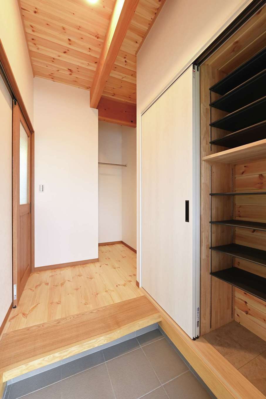 住まいるコーポレーション【収納力、趣味、自然素材】天然木の味のあるフォルムを生かした耳付き框が、高級感をもたらす玄関。土間の脇には収納スペースがあり、靴やゴルフバッグなどのアウトドア用品をしまえる。玄関ホールの奥には、外着をかけるクロークも設けた