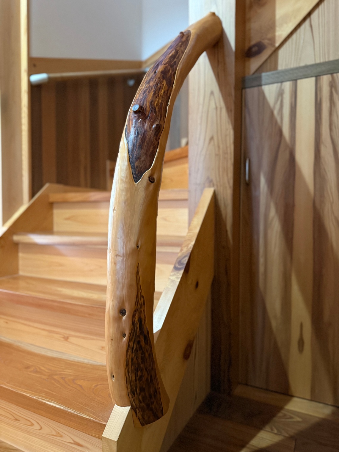 櫻 工務店【和風、自然素材、高級住宅】自然の曲りを活かしたムロの木の手すりがアクセントの階段。各所に温かみのある木材が用いられ、空間に落ち着きと自然な雰囲気を与えている。