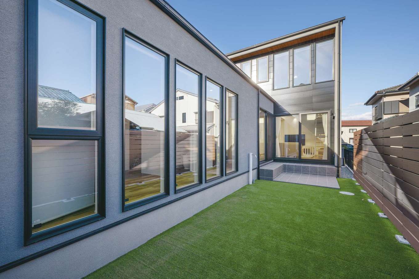 ハウスプラン（R＋house沼津・富士）【デザイン住宅、省エネ、建築家】玄関、駐車場とは反対側に設けた庭。メンテナンスコストを考えたリビングとの間はタイルデッキでつなぎ、一段下げたことで個性的な佇まいに
