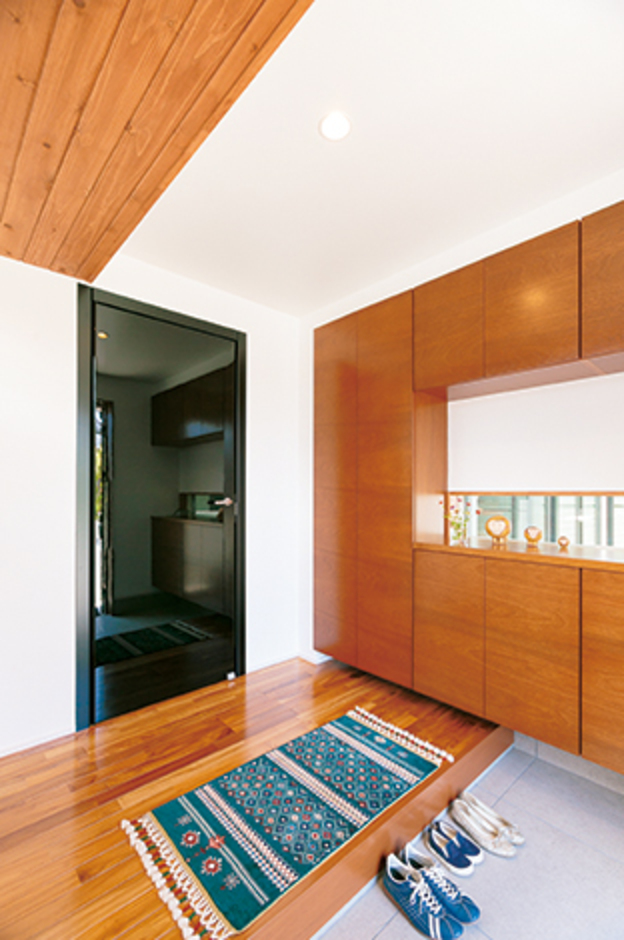 木のぬくもりのなかにモダンを感じる玄関ホール。中庭が見える鉄骨サッシのスリット窓はご主人のこだわり。納得オリジナルのイタリア製ドア「レーベル」の黒い輝きが差し色に