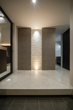 シンプルで上品なデザインの玄関スペース。暖色系の照明が壁面を柔らかく照らし、訪れる人をあたたかく迎える雰囲気を演出している。