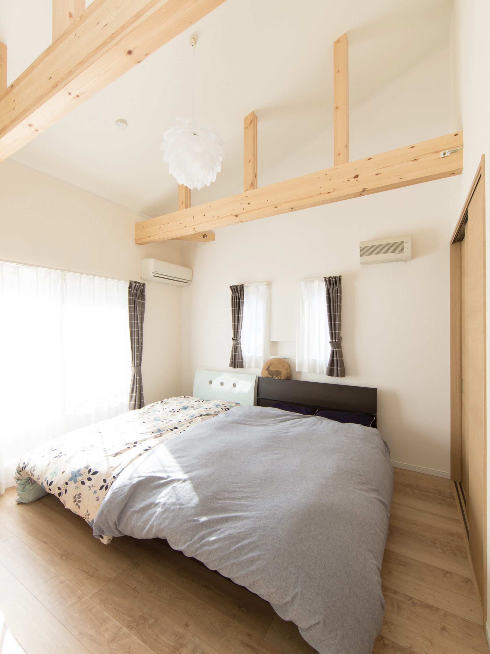 エスホーム｜片流れ屋根の特徴を活かした勾配天井で開放感のある寝室。ナチュラルウッドの梁がアクセントとなり、柔らかな日差しが降り注ぐ心地よい空間。