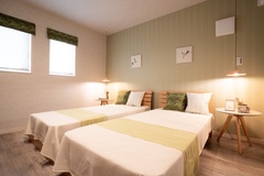 柔らかな照明に包まれたツインベッドが置かれた寝室。壁にはシンプルなアートが飾られ、落ち着いた雰囲気を演出している。