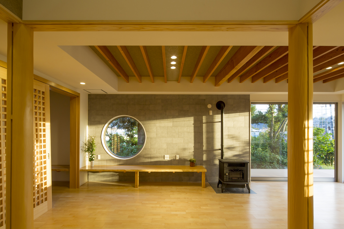 一級建築士事務所 GO_AN (ゴアン)【デザイン住宅、和風、建築家】夕日に染まるLDK。高台にあるので大きなサッシから光がよく入り明るく風通しもよい。天井が高いので空間がとても広く感じられる。調湿消臭効果のあるエコカラットタイルの壁にはめ込まれた丸窓が空間のアクセント