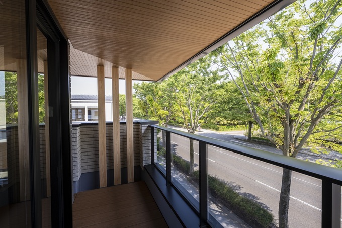 緑豊かな通りに面した開放的なバルコニー。ガラス手すりを用いて視界を遮らず、自然を感じられる設計が魅力的。木目調の天井が温かみを加えている。
